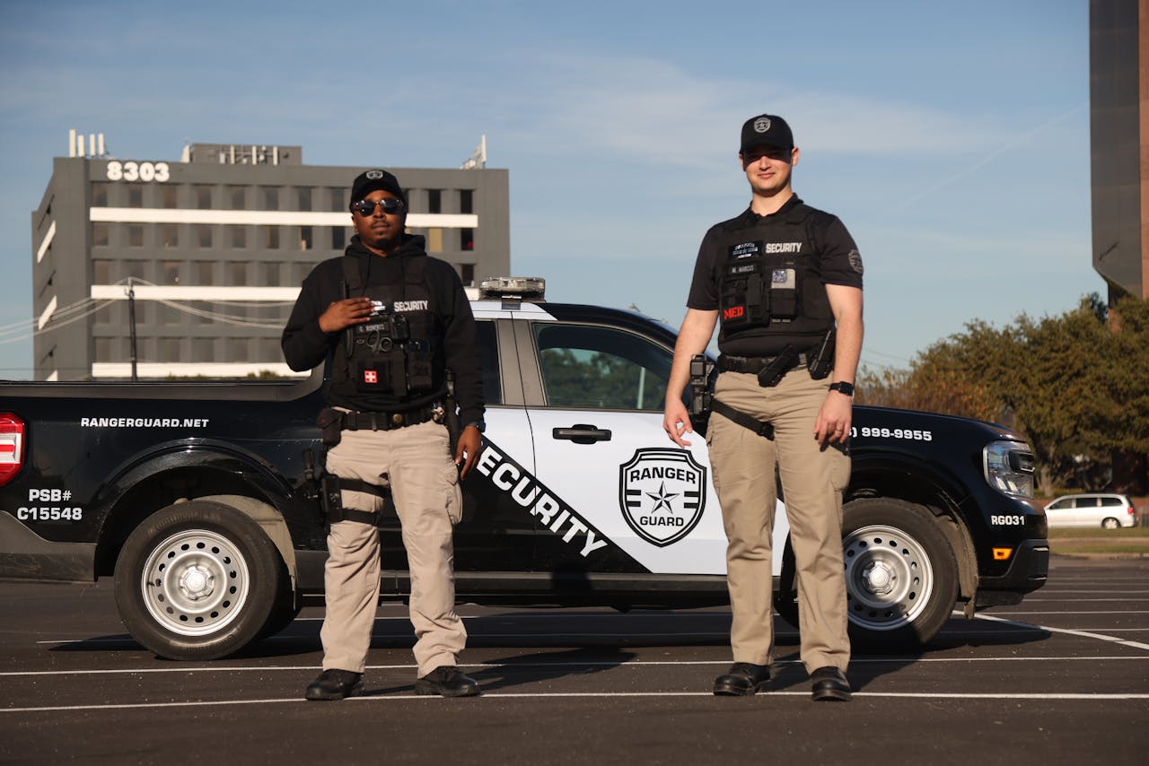 Two security officers in uniforms posing by a marked patrol vehicle outdoors.